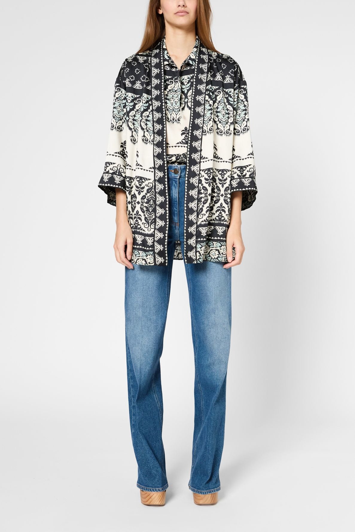 A person wearing a black and white patterned kimono-style jacket, light blue high-waisted jeans, and tan shoes stands against a plain white background.