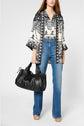 Woman wearing a patterned kimono-style top, high-waisted blue jeans, and tan platform shoes, holding a large black handbag against a plain background.
