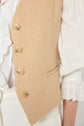 A close-up of a person wearing a beige gilet sans manche with four buttons over a white, lace-trimmed blouse with puffed sleeves and eyelet detailing. The gilet court, crafted from coton et lin, highlights both style and comfort. Only the torso and part of one arm are visible.