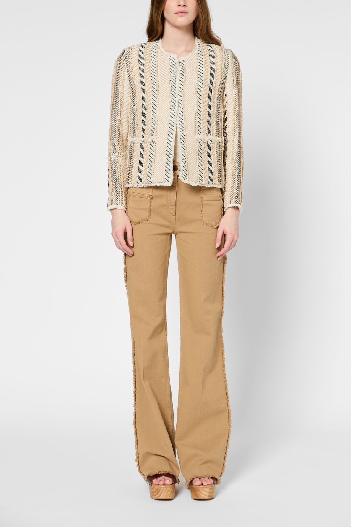 Person wearing a textured cream and blue striped jacket with front pockets, tan wide-leg pants with patch pockets, and platform sandals, standing against a plain white background.