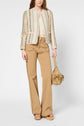 Woman wearing a textured cream and beige jacket, cream top, high-waisted tan wide-leg pants, and platform sandals, holding a small tan handbag.