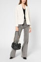 A woman wearing a white plaid blazer, black top, gray wide-leg jeans, and black shoes holds a black handbag with a gold chain. The image is cropped at the forehead.