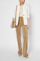 A woman wears a white jacket, beige top, high-waisted tan patterned pants, nude platform sandals, and carries a tan shoulder bag. She stands facing forward against a plain background.