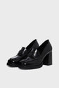 A pair of shiny black mocassin femme en cuir with chunky talon carré heels and stitched detailing, displayed against a plain light gray background.