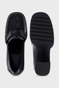 Top and bottom views of a pair of shiny black loafers en cuir. The left shoe shows the upper and penny strap detail reminiscent of a classic mocassin femme, while the right shoe displays the textured, ridged sole and distinctive talon carré. Both shoes are on a white background.
