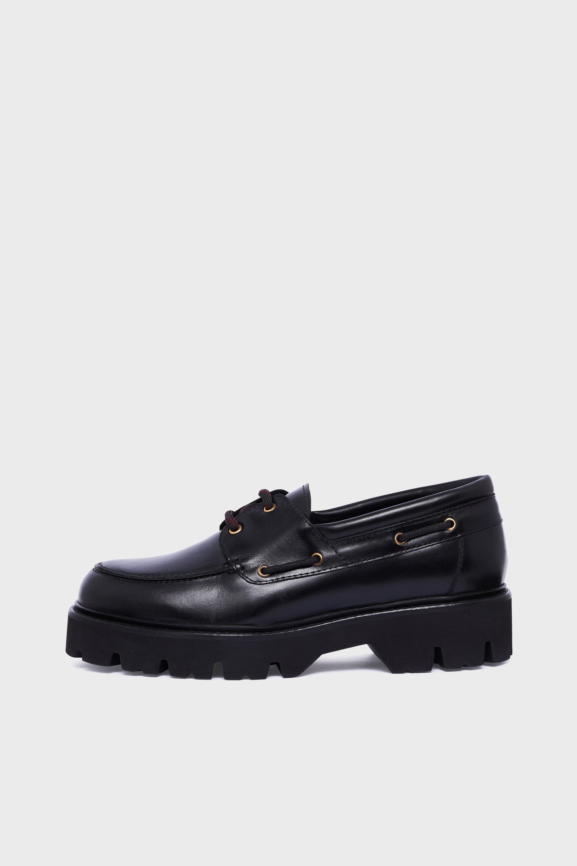 Black leather loafer, or mocassin cuir, with gold eyelets, lace detailing, and a thick semelle crantée for added grip, shown in profile on a plain light gray background.