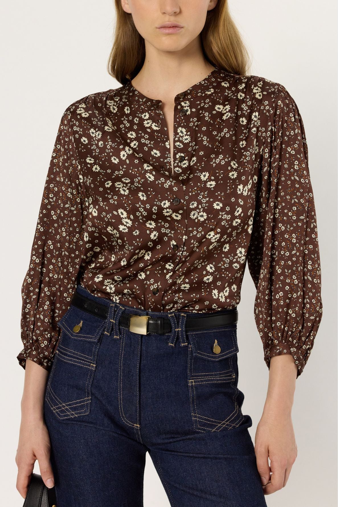 Woman wearing a brown chemise à fleurs with a round neckline and three-quarter sleeves, tucked into high-waisted, dark blue jeans with contrast stitching and a black belt.