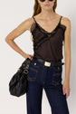 Woman in a lingerie chic black lace-trimmed camisole, high-waisted blue jeans with contrast stitching, and black belt, holding a black handbag. She has long wavy hair and wears large black sunglasses.
