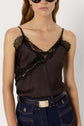 Woman wearing black sunglasses, a dark lace-trimmed satin dentelle camisole, high-waisted blue jeans with visible stitching, and a black belt with a gold rectangular buckle. The background is plain white.