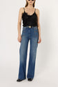 A person wearing a chic top noir satin camisole with dentelle trim, high-waisted wide-leg blue jeans with front pockets, a black belt, and black shoes, standing against a plain white background for an effortlessly elegant lingerie chic look.