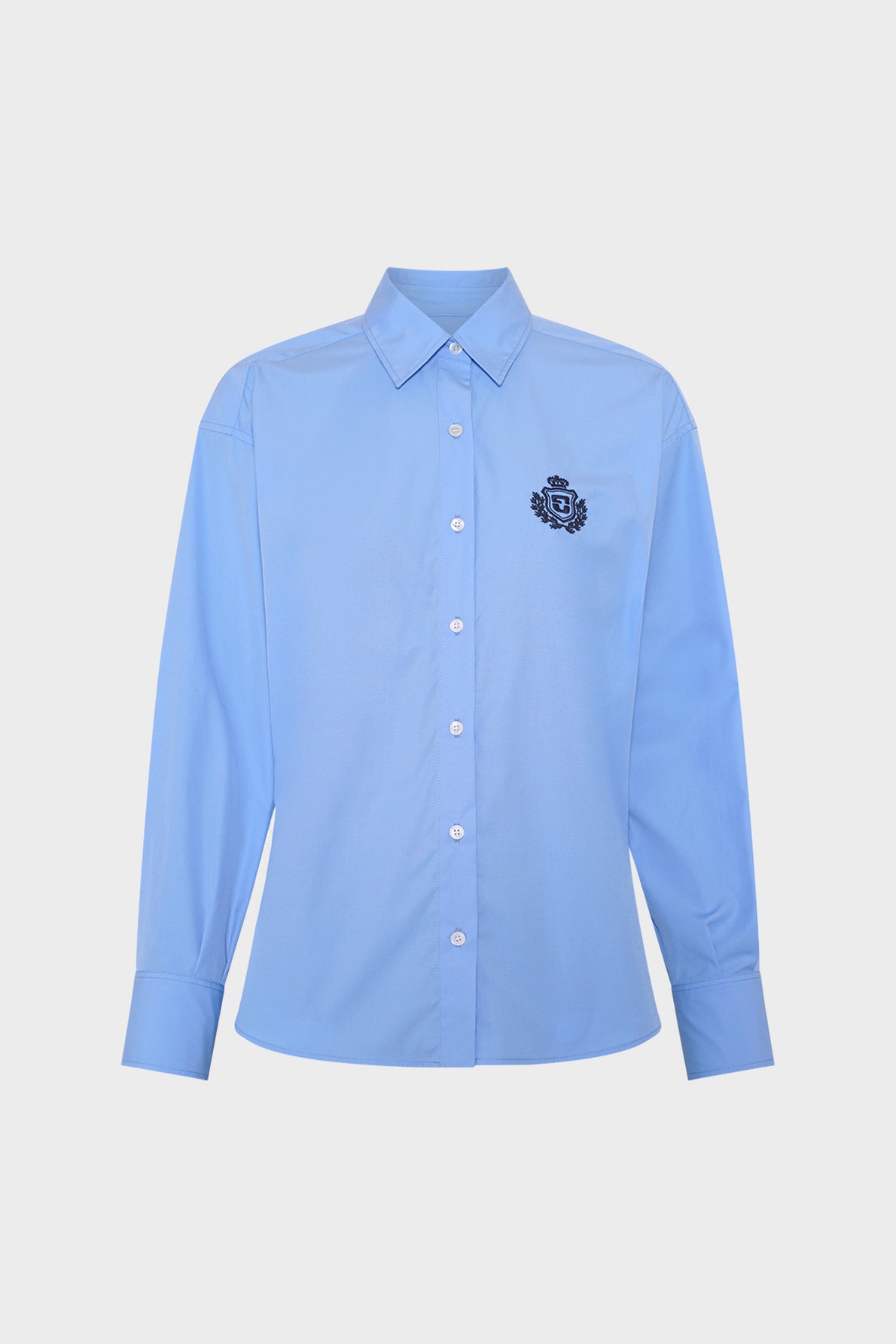 A light blue, long-sleeve button-up shirt with a pointed collar and a dark embroidered crest logo on the left chest, displayed on a plain white background.