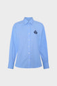 A light blue, long-sleeve button-up shirt with a pointed collar and a dark embroidered crest logo on the left chest, displayed on a plain white background.