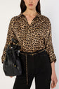Woman wearing a chemise léopard with black high-waisted pants, carrying a black leather drawstring bag with gold accents and a gold chain belt. The background is white.