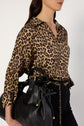 Woman wearing a chemise satinée imprimé léopard tucked into high-waisted black pants, accessorized with a gold chain belt and carrying a large black leather bag. Her head is turned slightly to the side.