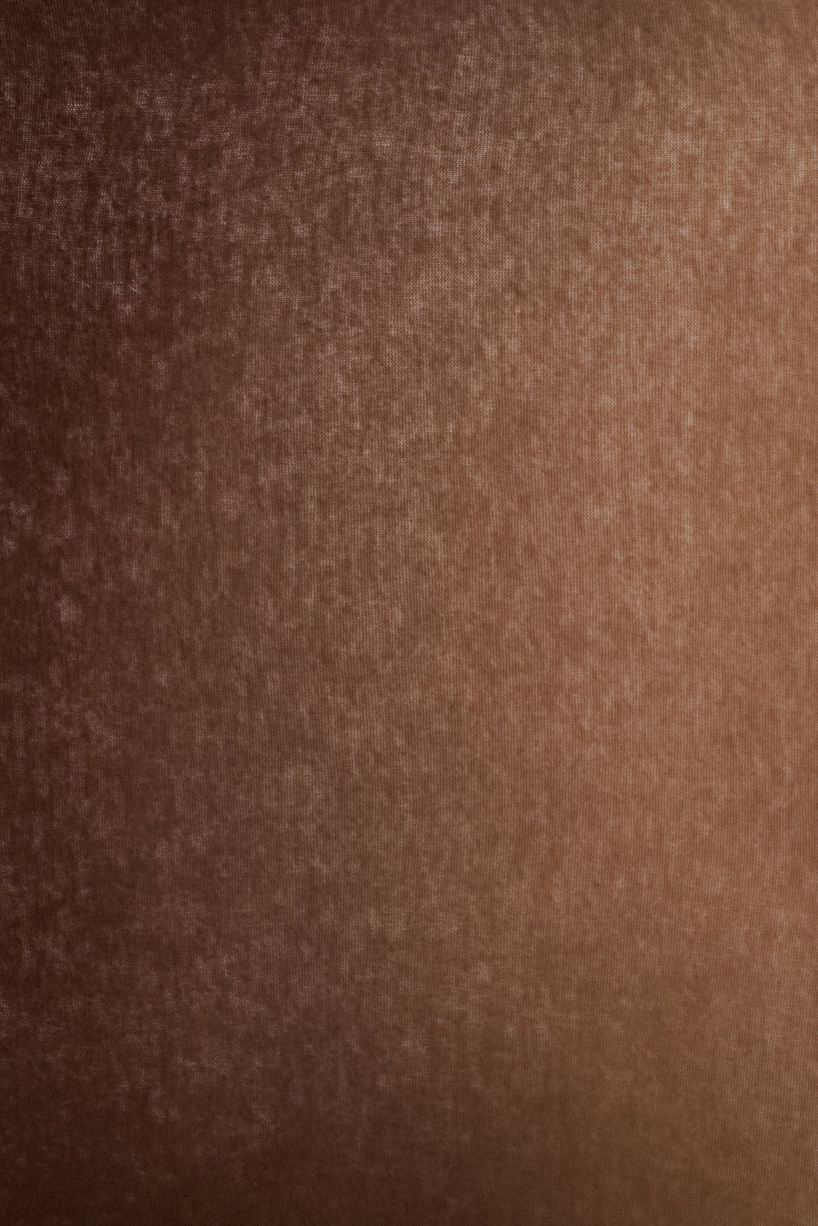 A close-up of a brown textured fabric surface, resembling an élégante écharpe marron, shows a soft, slightly mottled appearance with gentle shading and a subtle weave pattern, evoking the luxurious feel of an écharpe laine cachemire for femme.