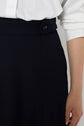 A person wearing a white long-sleeve shirt tucked into high-waisted black pants with a visible button detail on the waistband, reminiscent of the structured style of a jupe évasée. Only the torso and right hand are shown.
