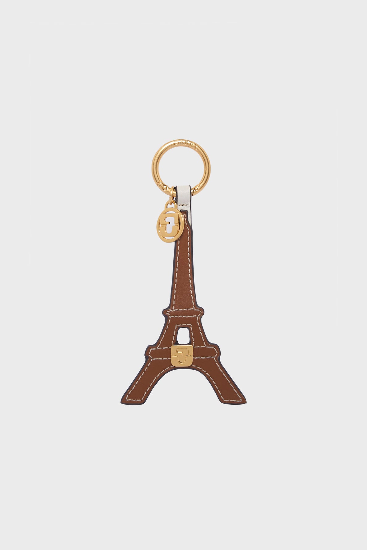 A brown leather porte-clé tour Eiffel keychain shaped like the iconic tower, crafted from premium cuir de vachette with white stitching and gold metal accents, including a circular key ring and a small charm, exuding pure élégance parisienne.