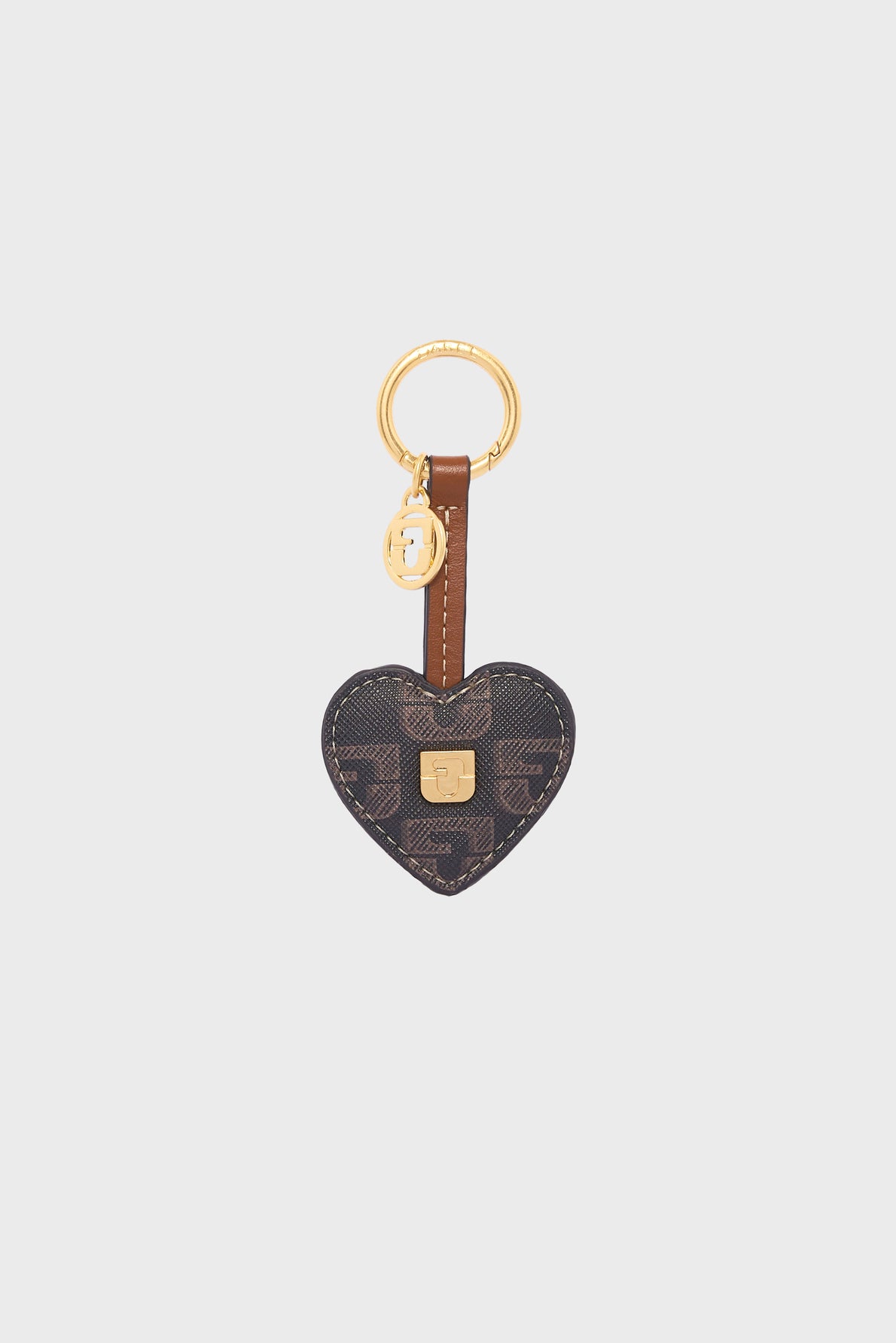 Heart-shaped keychain with dark patterned toile enduite monogrammée material, brown leather strap, gold-tone key ring, and a small golden lock detail in the center. A small round gold charm de sac hangs next to the key ring.