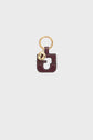 A gold keyring with a burgundy leather charm shaped like a square with a cutout. A small round gold tag, or médaille GD, featuring the iconic G logo hangs beside the charm, reflecting the timeless elegance of Gerard Darel’s porte-clé cuir accessories.