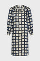 A knee-length robe courte femme with three-quarter sleeves, featuring a black and blue grid pattern on an off-white background. This robe imprimé géométrique has a loose fit and a small V-neckline, perfect for adding a touch of chic to your everyday style.
