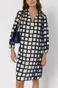Woman wearing a robe courte femme featuring a bold blue, black, and white geometric square pattern, holding a navy quilted handbag with a gold chain strap.