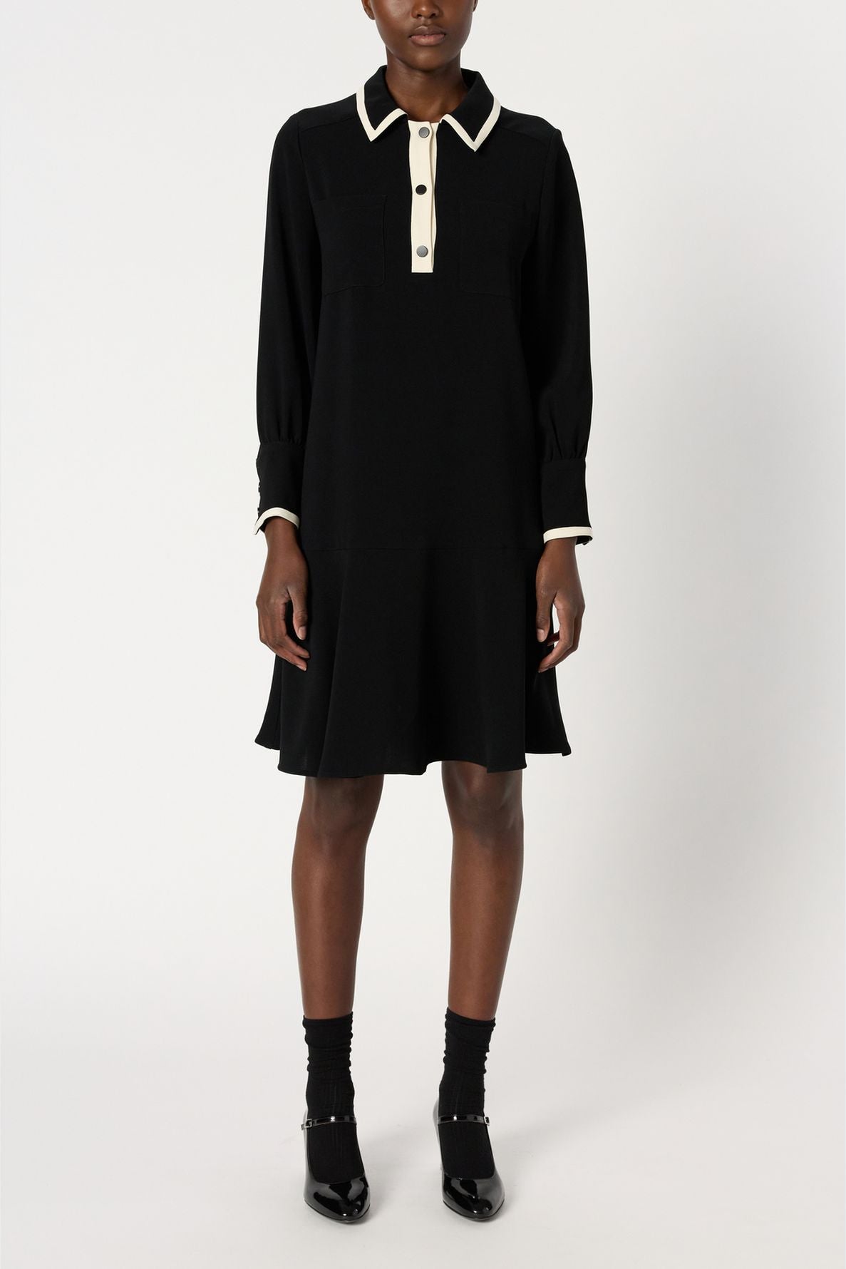 A person wearing a black robe courte chic with white trim on the collar and cuffs, black socks, and black shoes, standing against a plain white background.