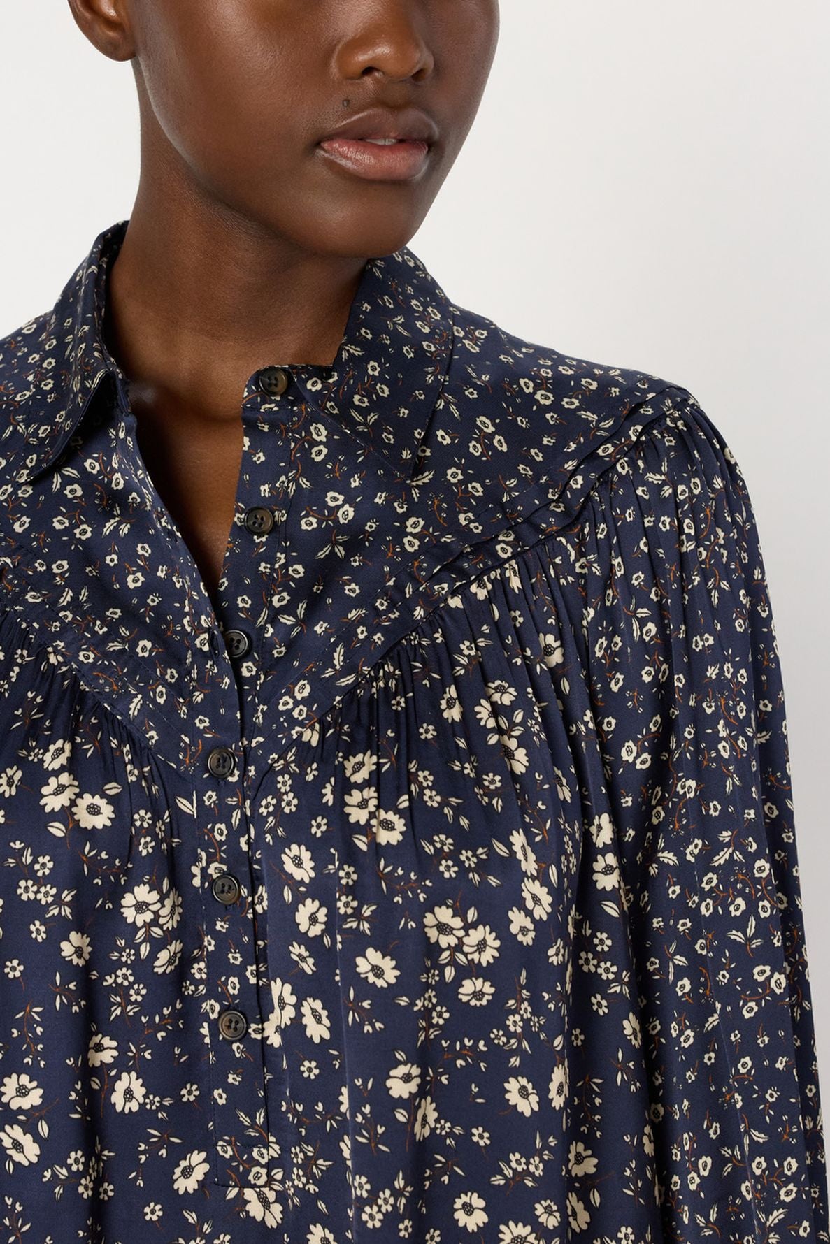 A person wearing a navy blue blouse with white floral patterns and black buttons, reminiscent of a robe satinée fleurs. Only the lower face, neck, and upper torso are visible.