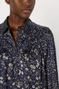 A person wearing a navy blue blouse with white floral patterns and black buttons, reminiscent of a robe satinée fleurs. Only the lower face, neck, and upper torso are visible.