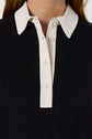 Close-up of a person wearing a black shirt with a white collar and white button placket, reminiscent of a col chemise style. The shirt has three visible buttons, and the wearer’s neck and part of the hair are visible.