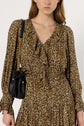 A woman wears a long-sleeved, ruffled robe léopard, styled as a robe longue with a chic silhouette, and carries a small black leather shoulder bag with a gold chain strap. Her face is partially visible, and the background is plain white.
