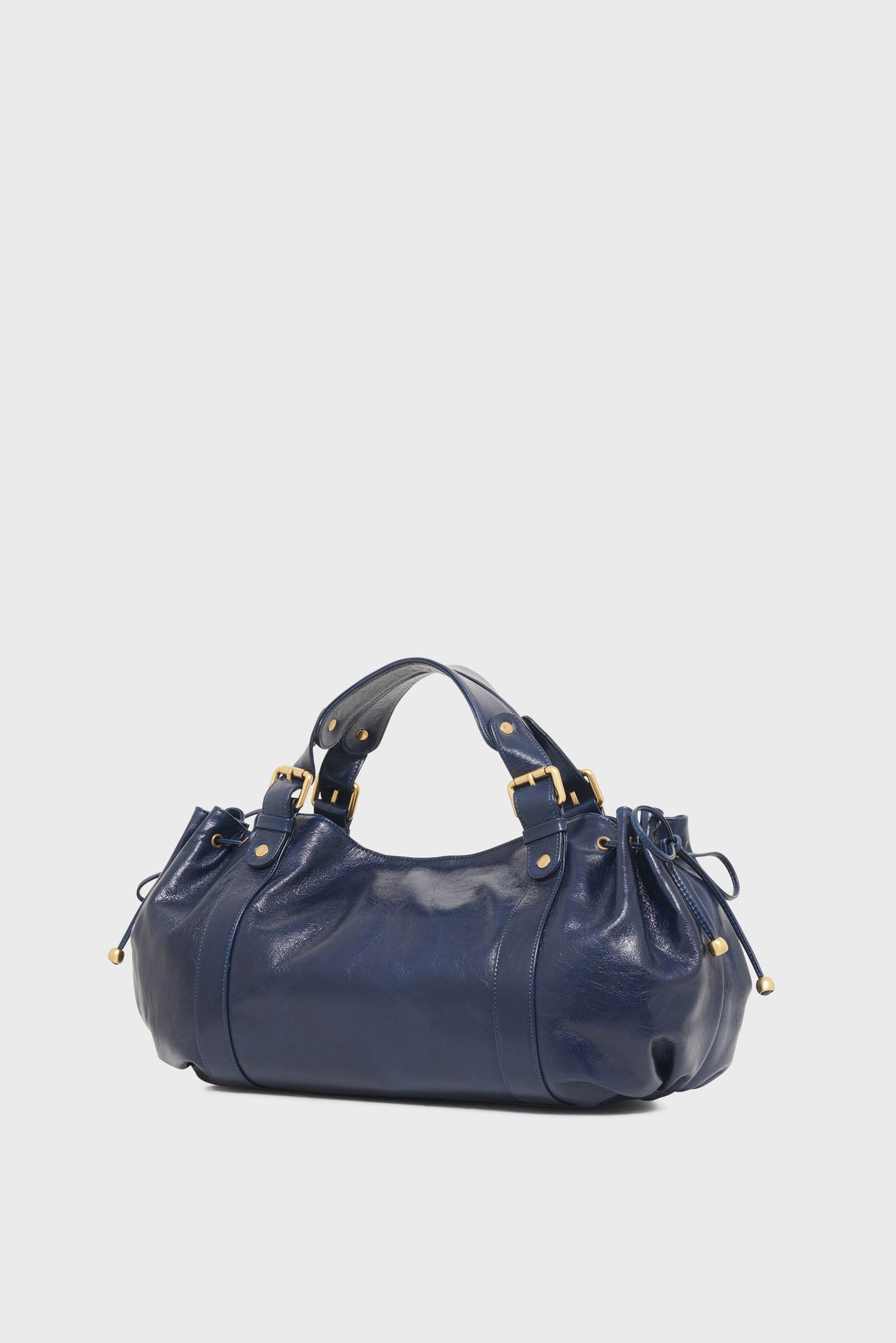 A shiny navy blue leather handbag, reminiscent of the iconic Vanessa Bruno sac à main cuir, with short handles, gold hardware, and side drawstring details, set against a plain white background.