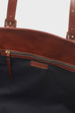 Close-up of an open brown leather sac porté épaule showing a zippered pocket and a fabric-lined interior.