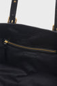 Interior of a black leather bag with gold metal hardware, inspired by the timeless elegance of a sac inspiration 70’s, featuring a zippered pocket and a fabric lining. The zipper pull is also black, and a stitched label is visible below the pocket, making this sac à main chic both stylish and practical.