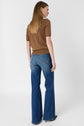 A woman with straight brown hair wears a brown short-sleeve top and blue flared jeans. She is standing and facing away, showing the back of her outfit against a plain white background.