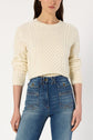 A woman wearing a pull écru en laine mélangée with subtle motifs géométriques and high-waisted blue jeans stands against a plain white background. Her face is partially out of frame.