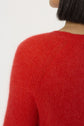 Close-up of a person wearing a fuzzy rouge baiser sweater in laine mélangée, showing the shoulder, upper back, and part of their head with short black hair. The background is plain and light-colored.