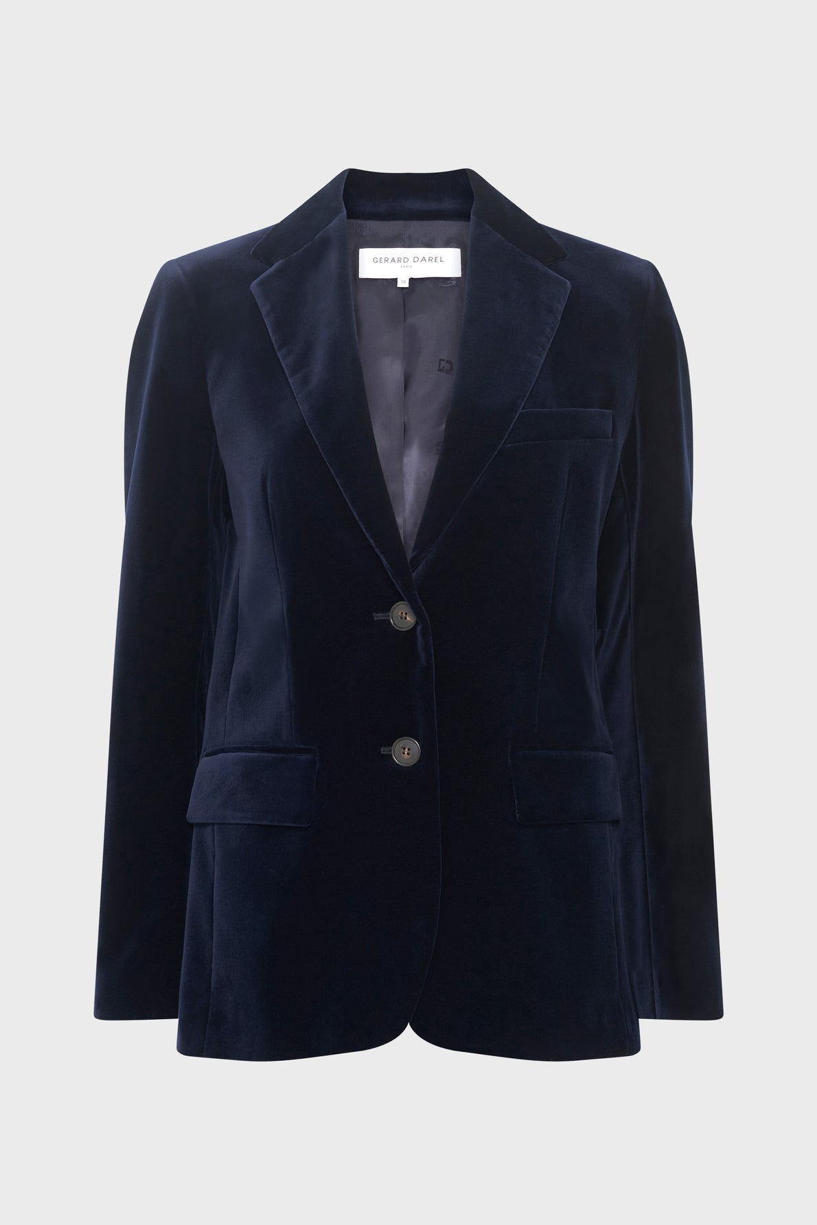 A navy blue velvet blazer, also known as a veste tailleur velours, with two buttons, front flap pockets, and a notched lapel is displayed against a plain light gray background. This veste bleu marine is the perfect choice for a veste femme chic look.