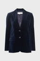 A navy blue velvet blazer, also known as a veste tailleur velours, with two buttons, front flap pockets, and a notched lapel is displayed against a plain light gray background. This veste bleu marine is the perfect choice for a veste femme chic look.