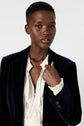 A person with short hair wears a veste bleu marine over a white shirt, looking at the camera with a neutral expression against a plain white background.
