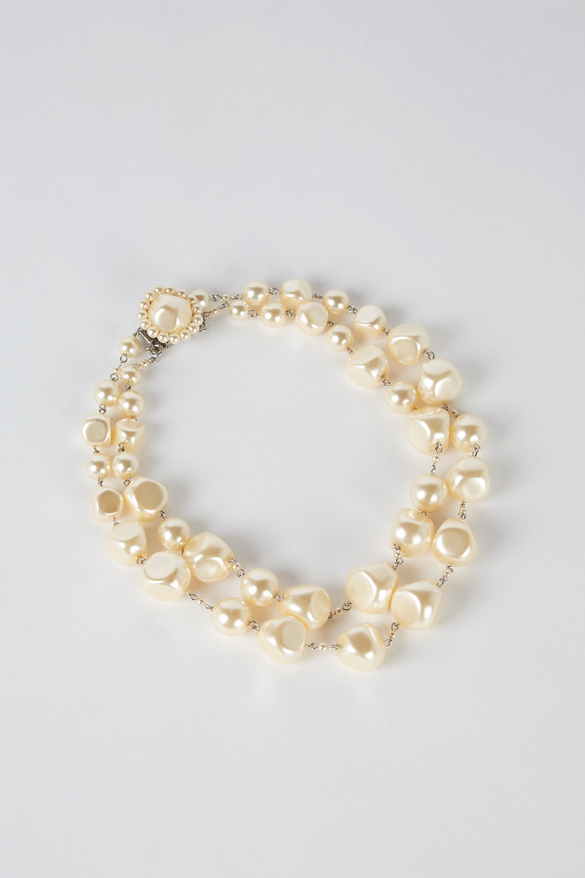 A collier double featuring irregularly shaped ivory pearls, round pearls, and perles de verre, completed with a decorative fermoir en métal, displayed on a plain white background.