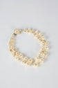 A collier double featuring irregularly shaped ivory pearls, round pearls, and perles de verre, completed with a decorative fermoir en métal, displayed on a plain white background.