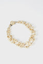 A collier double composed of irregular-shaped cream pearls and small round gold beads, featuring a decorative fermoir en métal, is elegantly displayed on a white background.