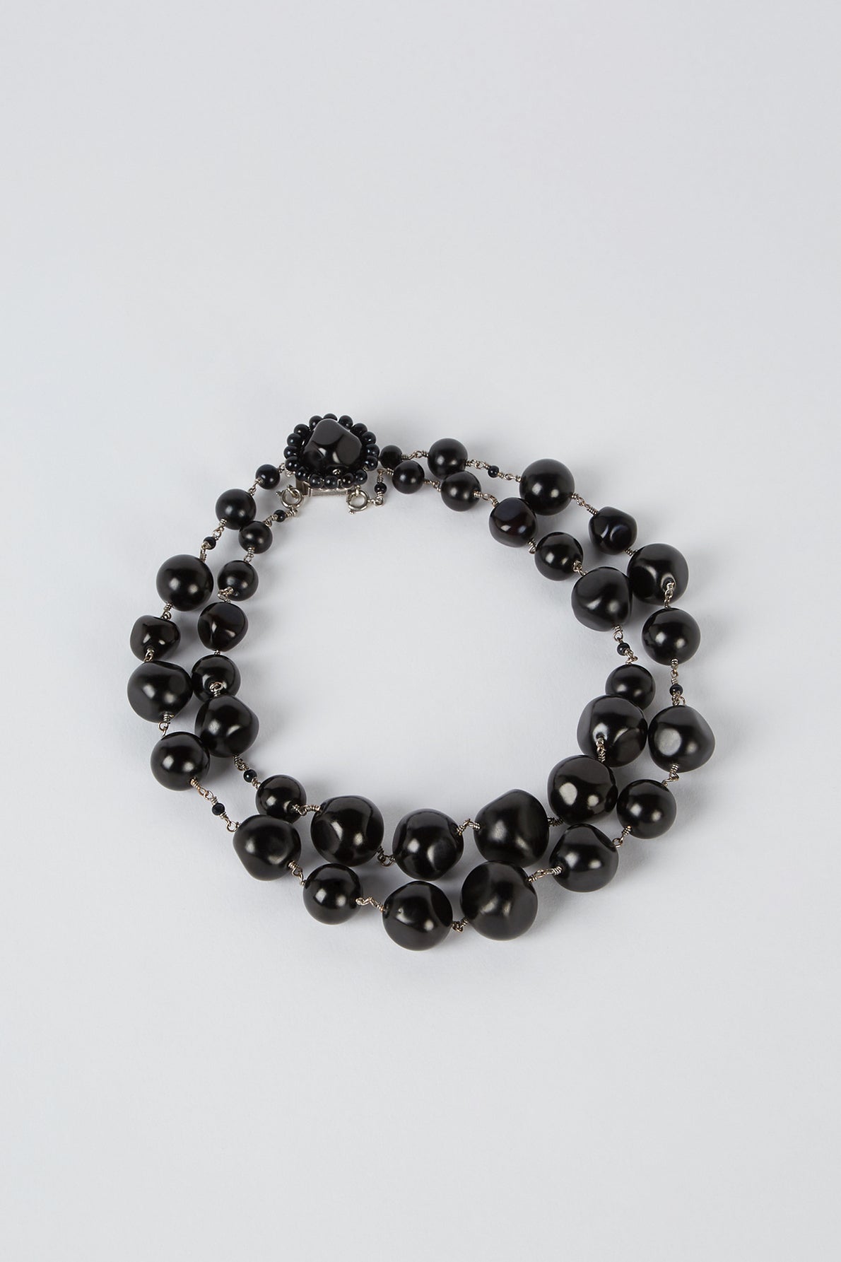 A double-stranded necklace made of round, glossy black beads with a decorative black clasp, displayed on a light gray background.
