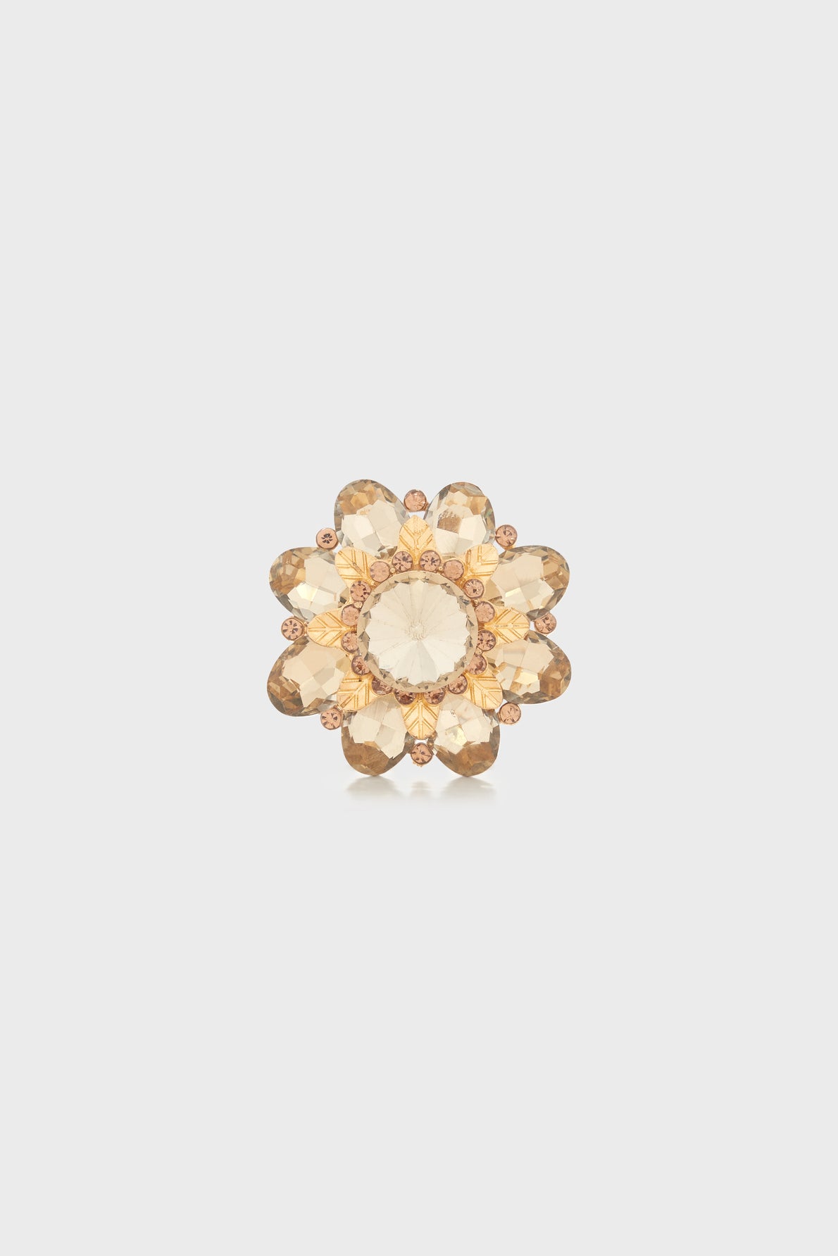 A gold-tone flower-shaped ring with faceted, light amber-colored gemstones arranged as petals and a large central stone evokes the elegant charm of a broche florale, set against a plain white background.