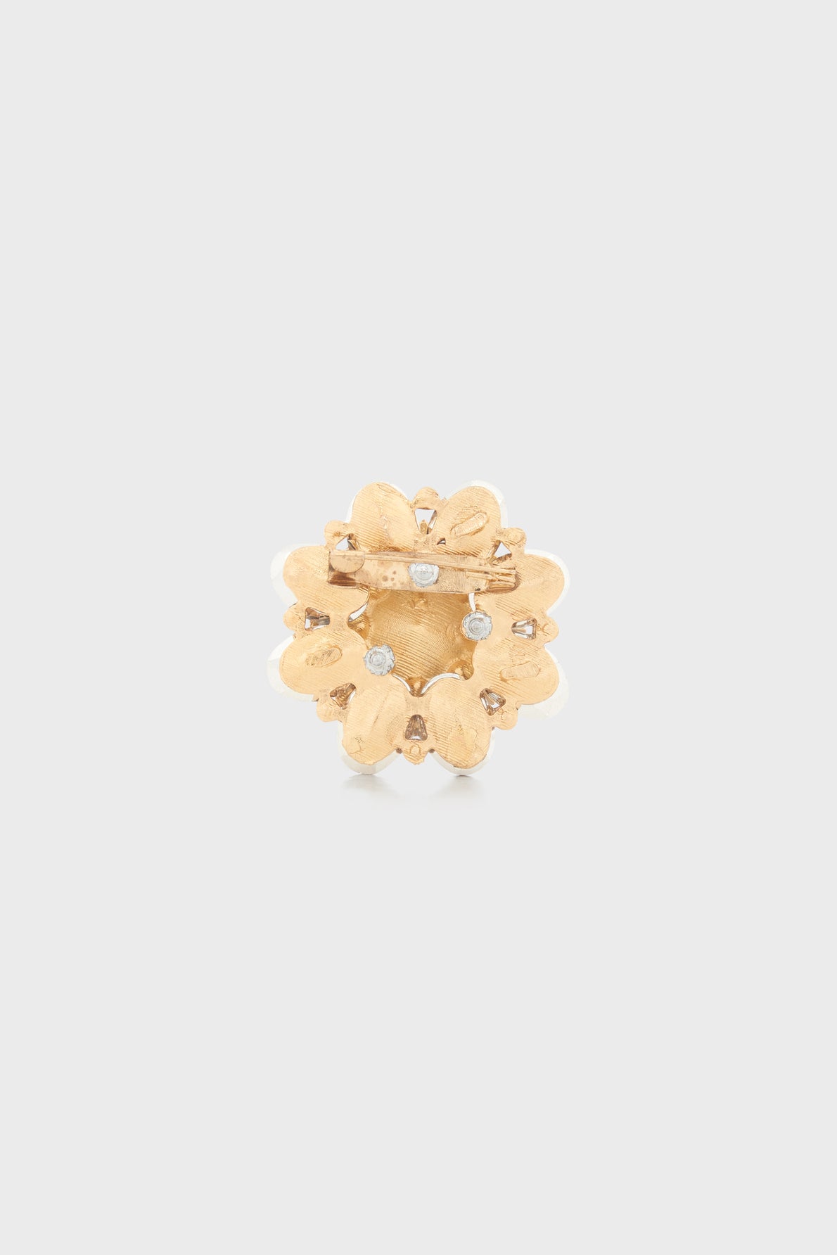 Gold flower-shaped brooch with textured petals and small clear gemstones. This elegant broche florale features a horizontal pin clasp at the back and is displayed on a plain light gray background.