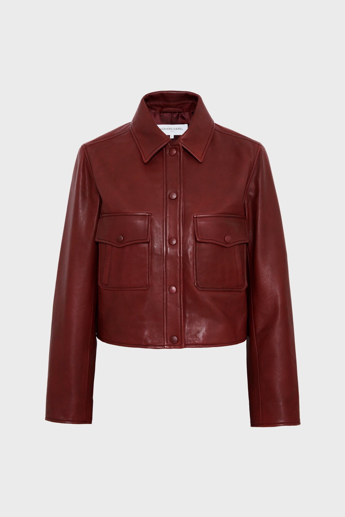 A cropped, long-sleeve, dark red leather jacket with a collar, front buttons, and two chest pockets, displayed on a plain light gray background.