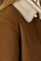 Close-up of a brown veste camel with a plush cream shearling collar and a ribbed knit underneath. The veste courte laine features a defined shoulder seam and a metallic button detail, offering both sophistication and warmth.