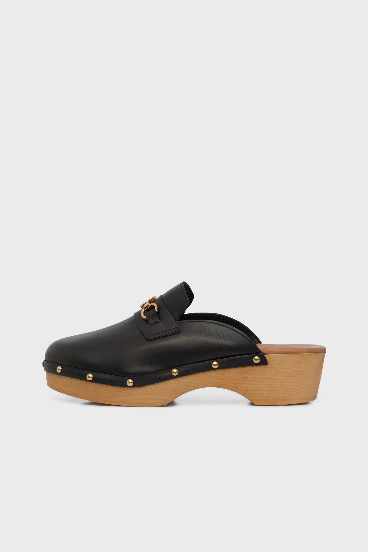 Ce sabot noir en cuir présente un talon en bois, des clous dorés et un mors siglé décoratif sur le dessus. Il est présenté en vue latérale sur fond blanc uni.