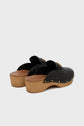 A pair of sabots noirs in black leather with wooden soles (talon en bois) and gold stud detailing, shown from the back on a light grey background.