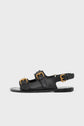 Black sandales cuir with two gold buckles on the front straps and one on the ankle strap, featuring a flat sole and an open heel. These elegant sandales à boucles are displayed on a plain light gray background.